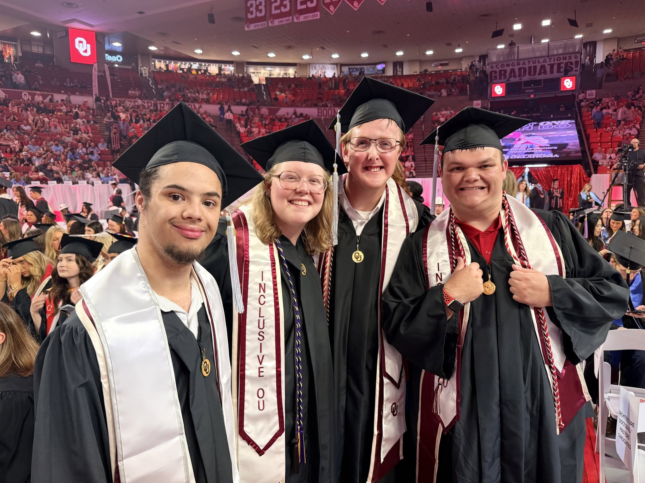 A group of students wearing graduation cap and gown standing in a large arena.