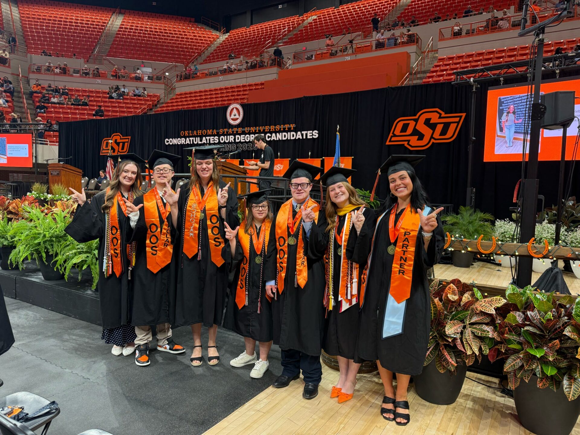 A group of opportunity orange students wearing graduation cap and gown standing infront of a graduation stage